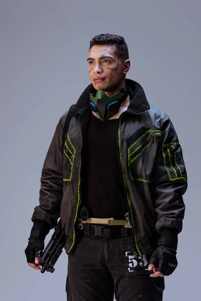Handsome and armed bi-racial cyberpunk player standing on grey — Stock Photo