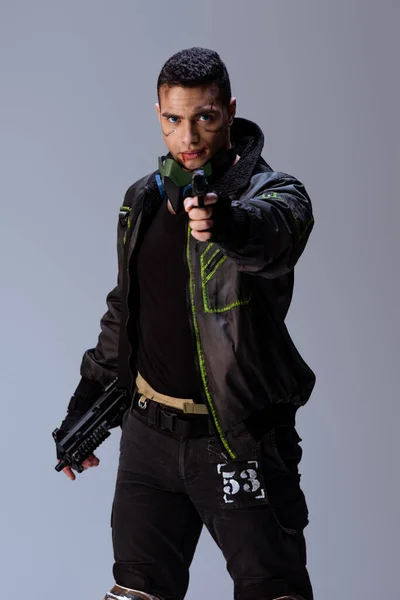 Guapo bi-racial cyberpunk jugador apuntando arma aislado en gris - foto de stock