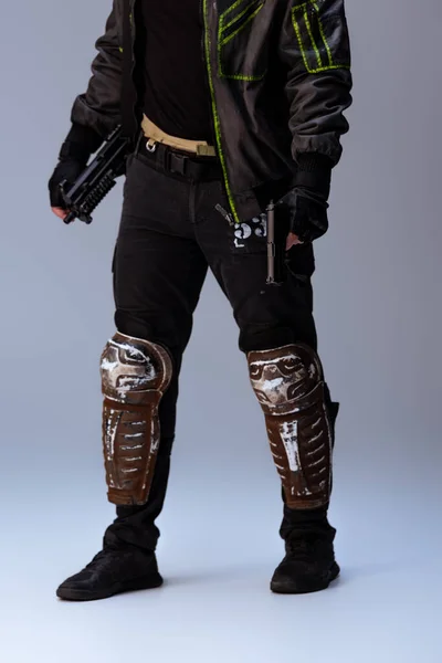 Vista recortada del jugador cyberpunk sosteniendo arma mientras está de pie en gris - foto de stock