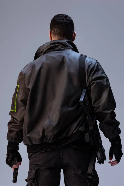 Back view of cyberpunk player holding gun while standing on grey — Stock Photo