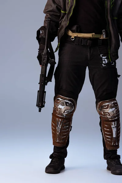 Vista recortada del jugador cyberpunk sosteniendo la pistola y de pie sobre gris - foto de stock