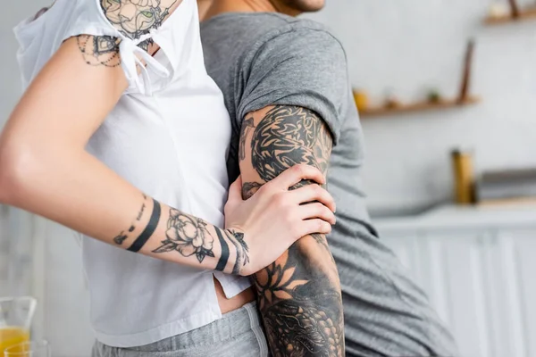 Cropped view of girl embracing tattooed boyfriend in kitchen — Stock Photo