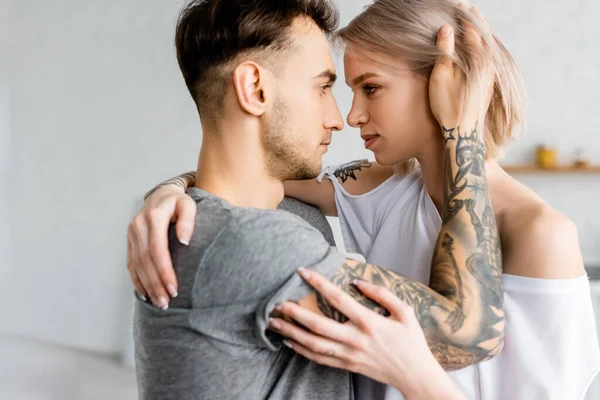 Vue latérale de belle femme embrassant petit ami tatoué à la maison — Photo de stock