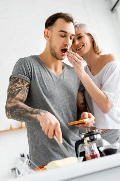 Selektiver Fokus einer lächelnden Frau, die tätowierten Freund während des Frühstücks in der Küche mit Trauben füttert — Stockfoto