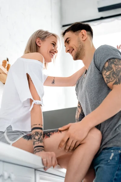 Low angle view of tattooed couple smiling at each other in kitchen — Stock Photo