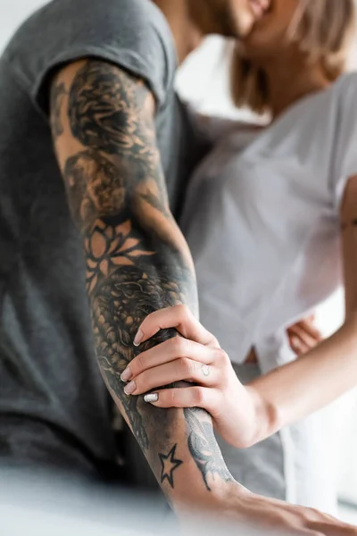 Enfoque selectivo de la mujer tocando la mano oh novio tatuado en casa - foto de stock