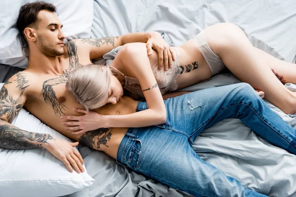 Top view of shirtless tattooed man embracing beautiful girl in underwear on bed — Stock Photo