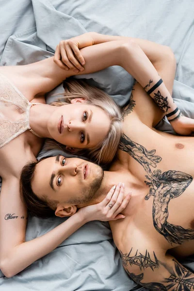 Вид зверху татуйованої пари дивиться на камеру, торкаючись один одного на ліжко — стокове фото