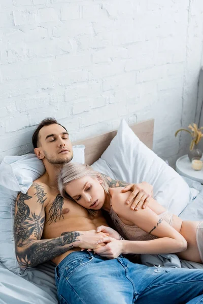 Привлекательная девушка в нижнем белье трогательная рука мускулистого татуированного бойфренда на кровати — стоковое фото