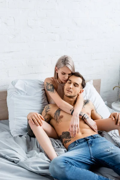 Mujer rubia en sujetador tocando sin camisa novio tatuado en la cama - foto de stock