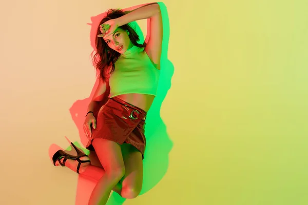 Top view of stylish, beautiful girl looking at camera while lying on yellow background with green and red shadows — Stock Photo