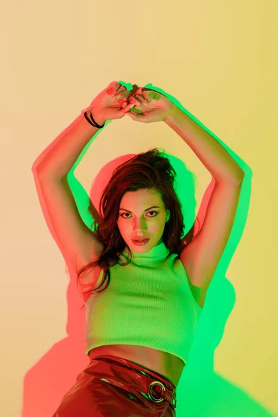 Vista superior de sensual, chica de moda mirando a la cámara mientras está acostado en el fondo amarillo con sombras verdes y rojas - foto de stock