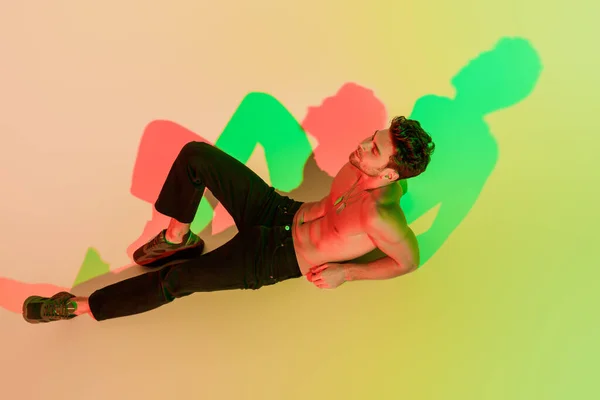 High angle view of sexy, dreamy man in black jeans lying with closes eyes on yellow with red and green shadow — Stock Photo