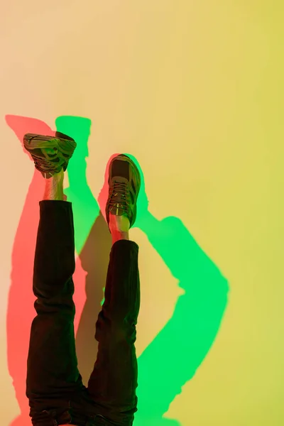 Cropped view of male legs in black jeans and sneakers on yellow with red and green shadows, top view — Stock Photo