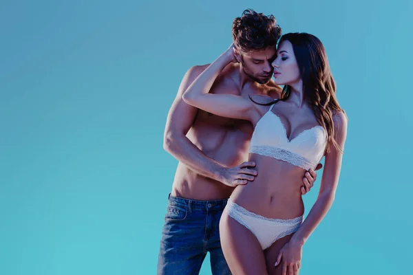Sexy Mann in Jeans und verführerisches Mädchen in weißen Dessous umarmen isoliert auf blau — Stockfoto