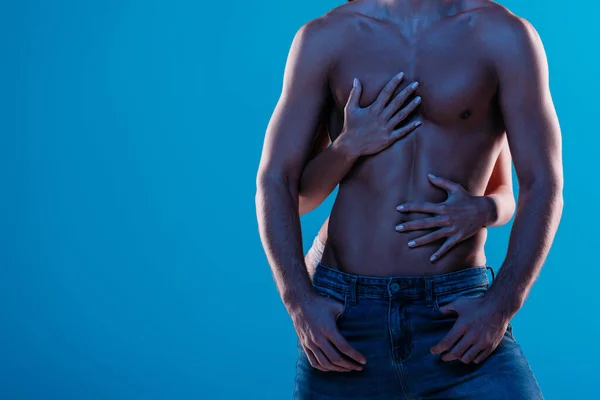 Cropped view of girl hugging sexy, shirtless man in blue jeans isolated on blue — Stock Photo