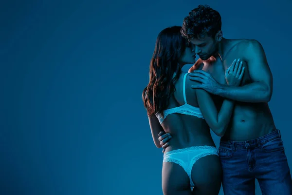 Sexy man in denim jeans embracing seductive girl in white lingerie isolated on dark blue — Stock Photo