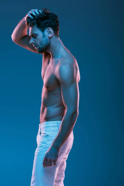 Vista laterale di sexy uomo premuroso in jeans bianchi testa toccante isolato su blu — Foto stock