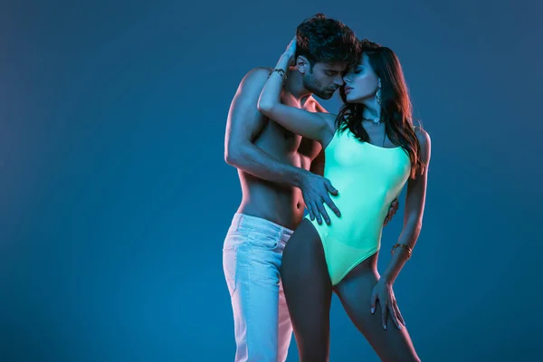 Handsome, shirtless man in white jeans and sensual girl in swimsuit embracing isolated on blue — Stock Photo