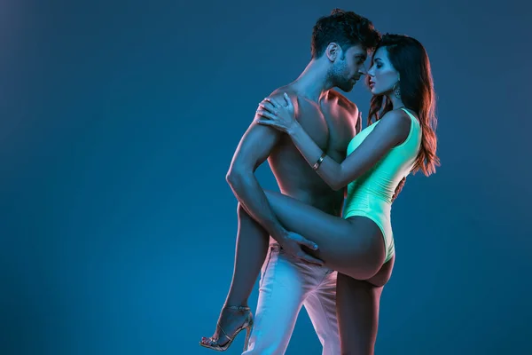 Shirtless man in white jeans and sexy girl in swimsuit embracing isolated on blue — Stock Photo