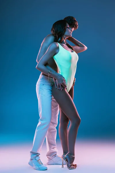 Full length view of sexy man in white jeans abraçando menina sedutora em maiô no fundo azul — Fotografia de Stock