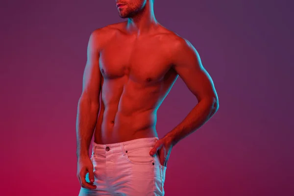 Частичный вид сексуального, без рубашки мужчина держит руку в заднем кармане, позируя на фиолетовом фоне с градиентом — стоковое фото