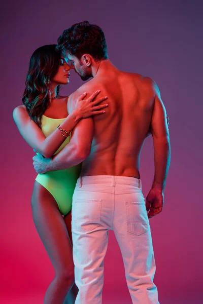 Back view de homem sem camisa sexy e menina sensual em maiô abraçando no fundo roxo — Fotografia de Stock