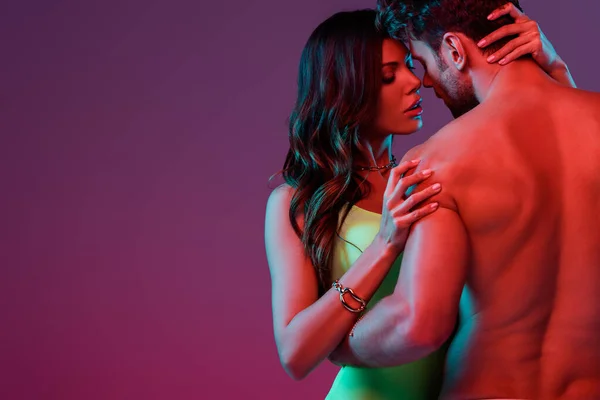 Back view of sexy shirtless man and seductive girl in swimsuit embracing on purple background — Stock Photo