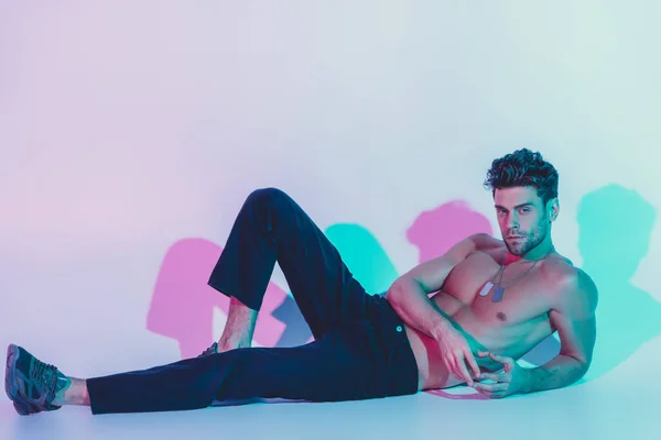 Sexy, confident man in dark blue jeans looking at camera while lying on blue background with shadows — Stock Photo