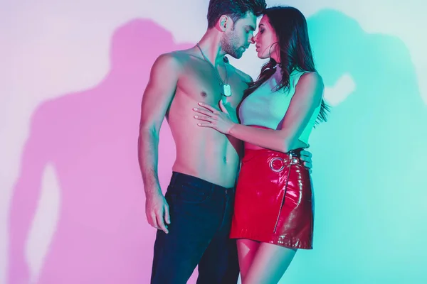 Sensual girl in red mini skirt and shirtless man in dark blue jeans hugging on background with turquoise and violet shadows — Stock Photo