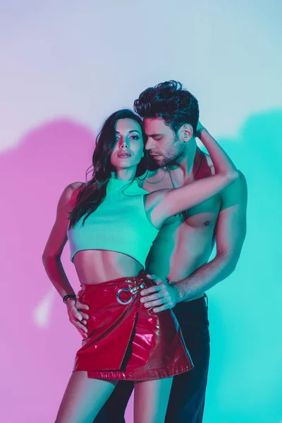 Sexy Mann berührt Hüften von sinnlichen Mädchen umarmt seinen Hals und blickt in die Kamera auf blauem Hintergrund mit türkisfarbenen und violetten Schatten — Stockfoto