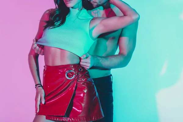 Cropped view of shirtless man touching top of seductive girl embracing hid neck on turquoise and violet background — Stock Photo