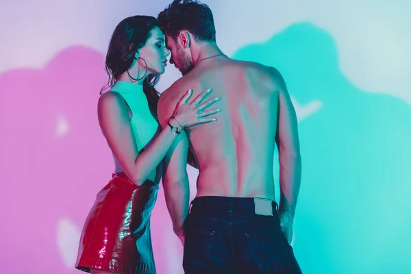 Sexy, stylisches Mädchen berührt hemdlosen Mann auf Hintergrund mit türkisfarbenen und violetten Schatten — Stockfoto