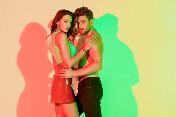 Happy young couple embracing while looking at camera on yellow background with red and green shadows — Stock Photo