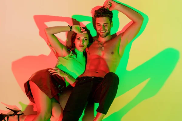 Sensual, trendy girl and sexy man smiling while lying on yellow background with red and green shadows — Stock Photo