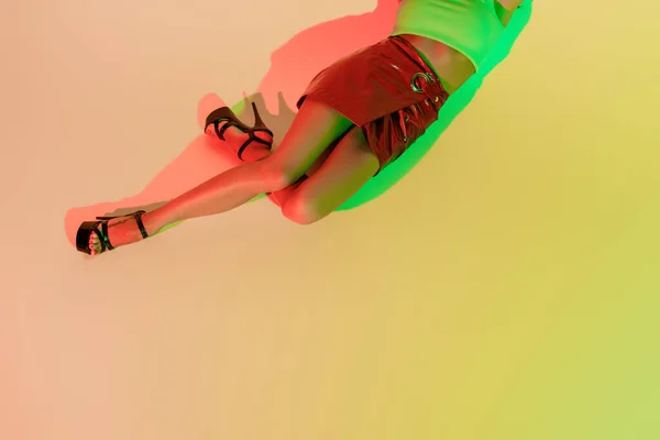 Обрезанный вид стильной девушки, лежащей на желтом фоне с зелеными и красными тенями — стоковое фото
