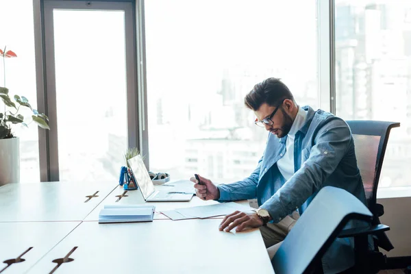 Travailleur informatique tenant un stylo et regardant les papiers à table dans l'espace de coworking — Photo de stock