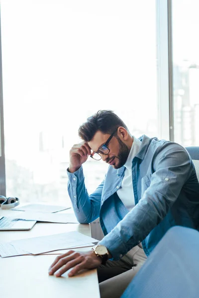 Trabajador de TI reflexivo mirando papeles en la mesa en el espacio de coworking - foto de stock