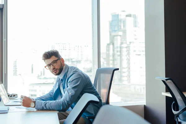 Enfoque selectivo del trabajador de TI mirando la cámara en la mesa en el espacio de coworking — Stock Photo