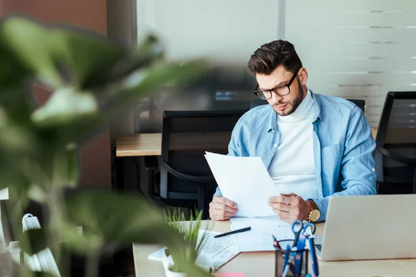 Selective focus of concentrated IT worker looking at papers at table in coworking space — Stock Photo