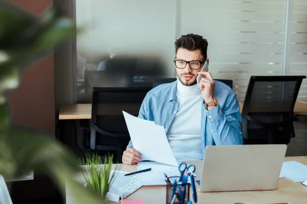 Focus selettivo del lavoratore IT con documenti che parlano su smartphone a tavola nello spazio di coworking — Foto stock