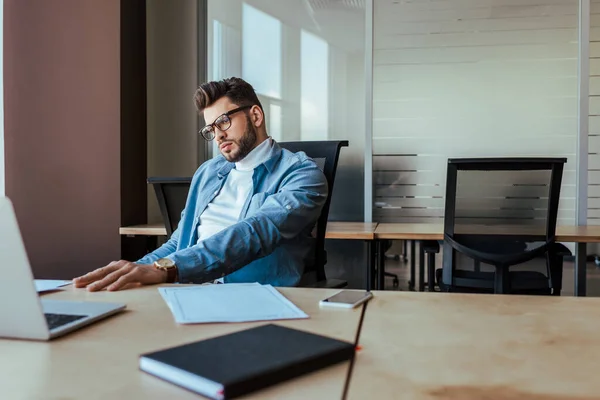 Enfoque selectivo del trabajador de TI reflexivo en la mesa en el espacio de coworking - foto de stock