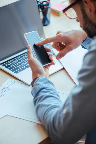 Selective focus of IT worker using smartphone at table with laptop and papers — Stock Photo