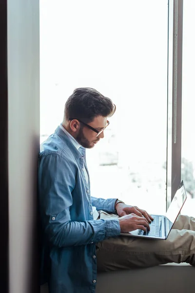 Lavoratore IT che utilizza laptop sul davanzale della finestra vicino alle finestre — Foto stock