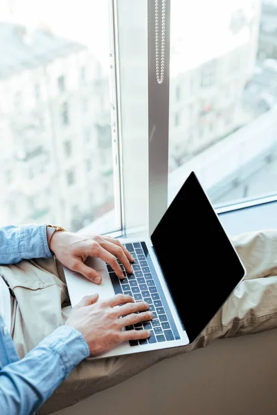 Vue partielle du travailleur informatique utilisant un ordinateur portable sur le rebord de la fenêtre près des fenêtres — Photo de stock