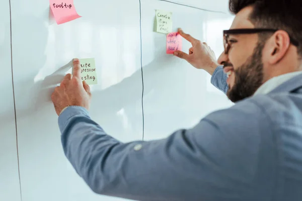 Selective focus of scrum master smiling and putting stickers on white board — Stock Photo
