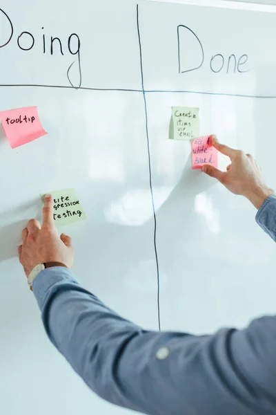 Cropped view of scrum master putting stickers on white board with spreadsheet with doing and done lettering — Stock Photo