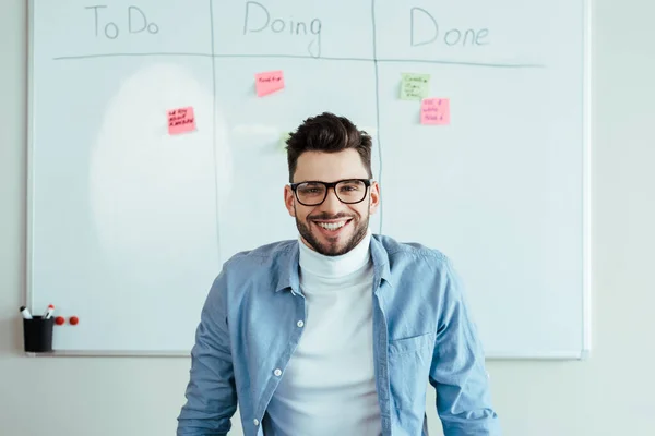 Scrum Master schaut in die Kamera und lächelt neben Whiteboard mit Aufklebern und Tabellenkalkulation mit zu tun, zu tun, zu tun, fertig Schriftzug — Stockfoto