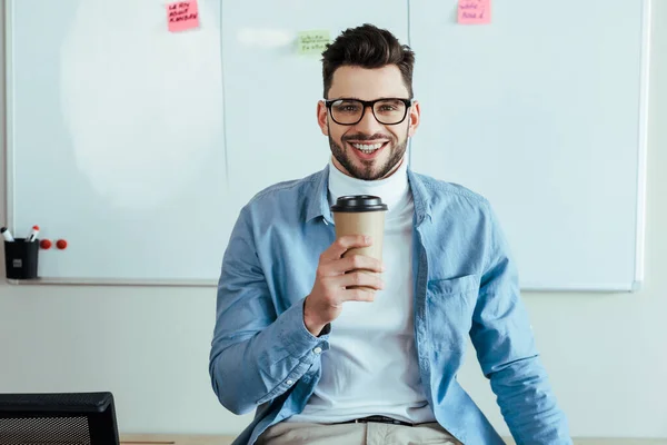 Scrum mestre olhando para a câmera e sorrindo com xícara de papel de café perto de placa branca com adesivos — Fotografia de Stock