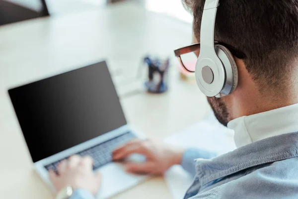 Enfoque selectivo del trabajador de TI en auriculares que trabajan con computadora portátil en el espacio de coworking - foto de stock